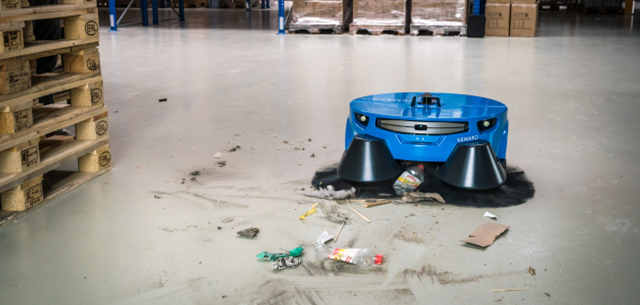 Cleaning robot in action sweeping up litter and trash on a warehouse floor